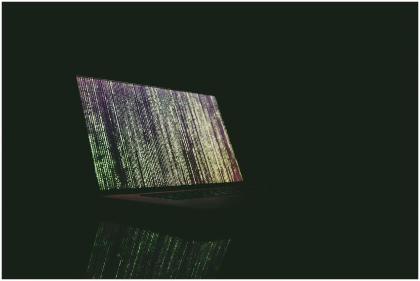 A laptop displaying green and purple code in a dar