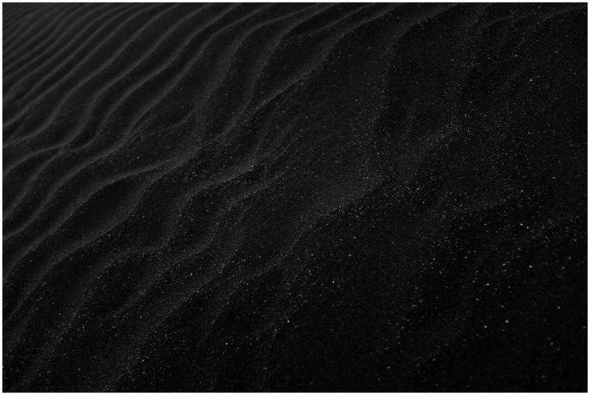 Textured black sand with ripples resembling dunes,