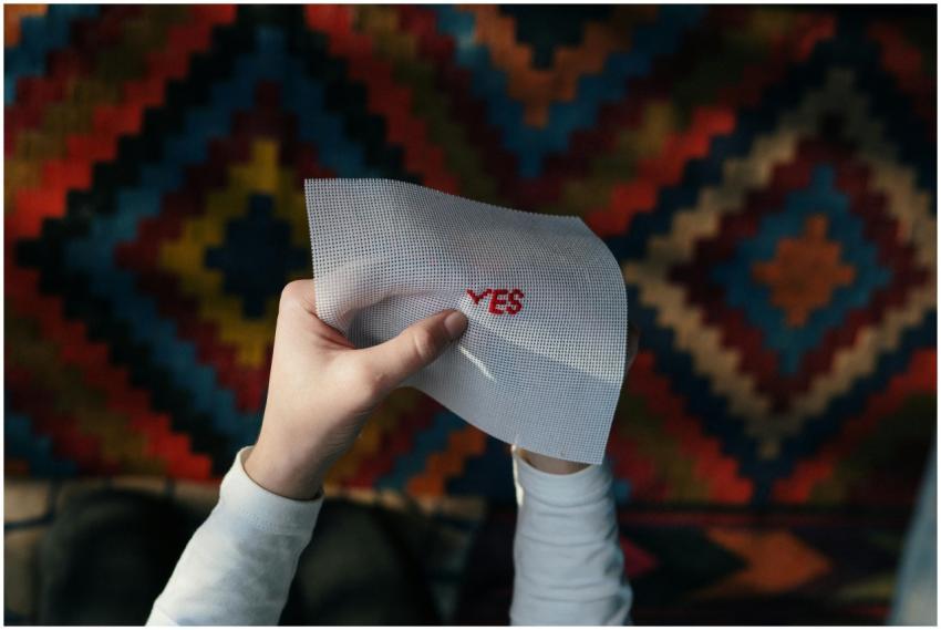 Hands holding an embroidered 'Yes' piece with colo