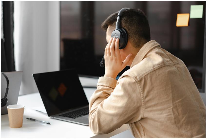 A man wearing headphones works at a laptop in a mo