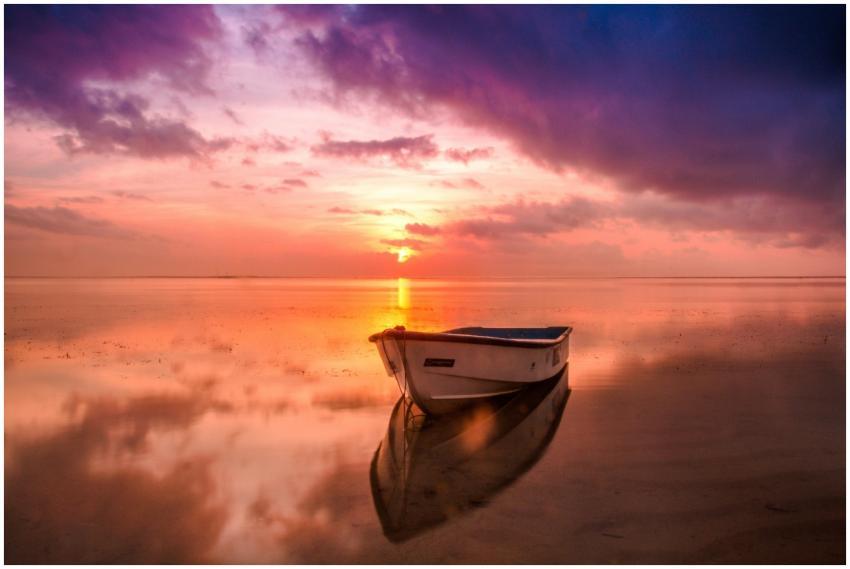 A tranquil scene of a boat at sunset with vivid sk