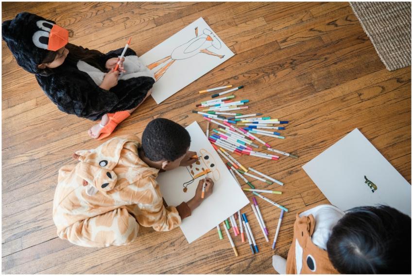 Kids in animal costumes lay on wooden floor drawin