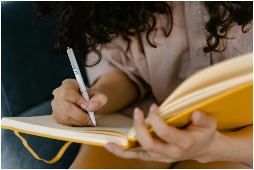 Person writing in a yellow notebook indoors, focus