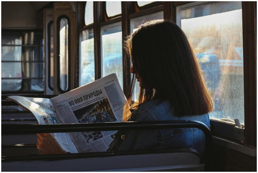 A woman reads a newspaper in a sunlit bus, capturi