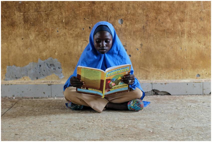 A young girl in hijab sitting on a floor reading a