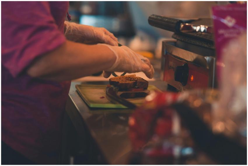 A chef wearing gloves prepares a sandwich indoors
