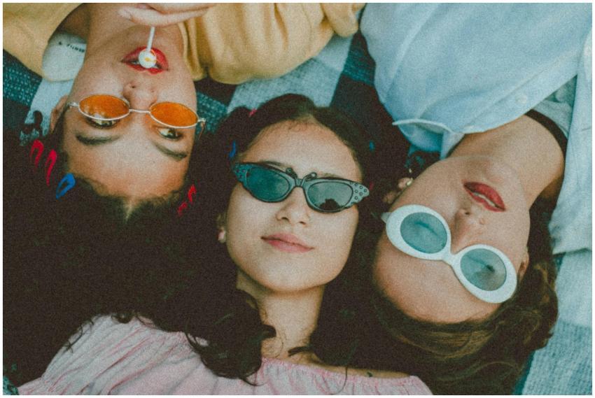 Three stylish women lying outdoors, wearing sungla