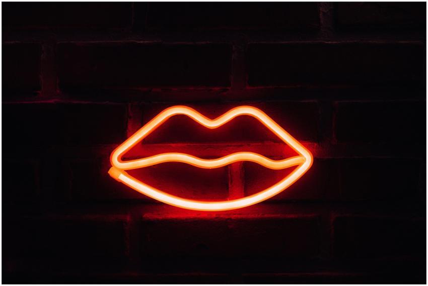 Illuminated neon lips wall art on a dark brick bac