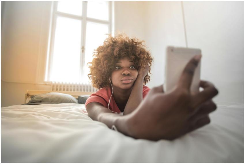 A young woman with curly hair lies on a bed, takin