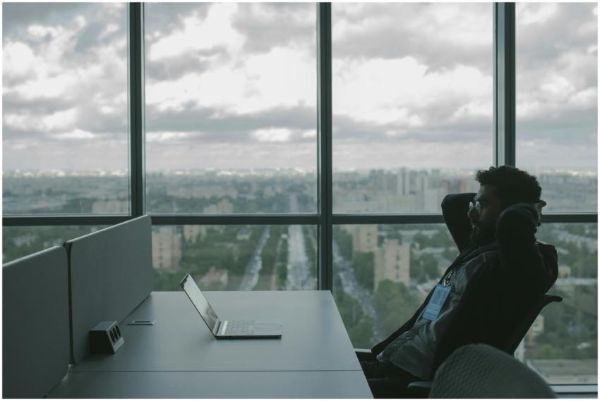 A man sits in an office with hands on head in fron