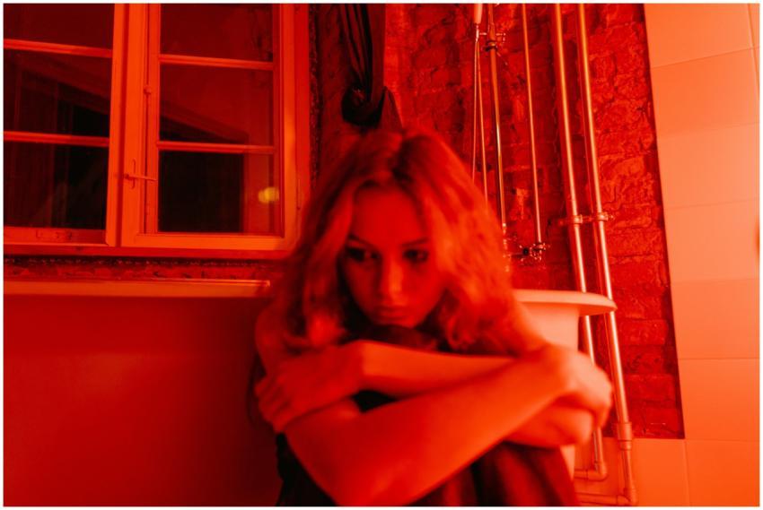 Woman sitting alone in a red-lit room, hugging her