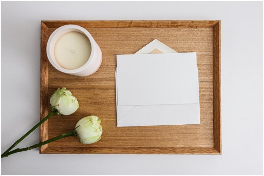 Flat lay of white envelope, flowers, and candle on