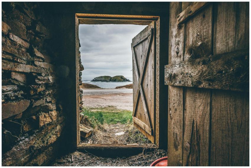 A rustic wooden doorway frames a picturesque beach