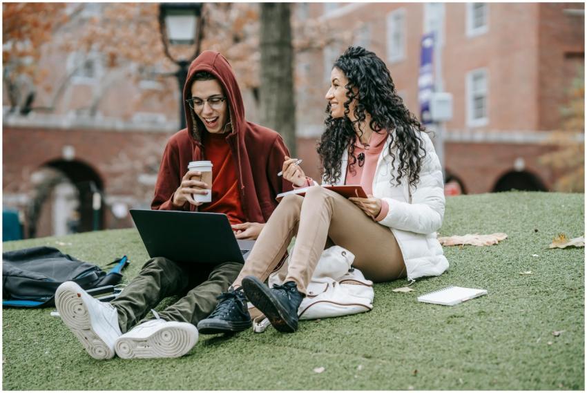 Two college students studying on campus lawn, enjo