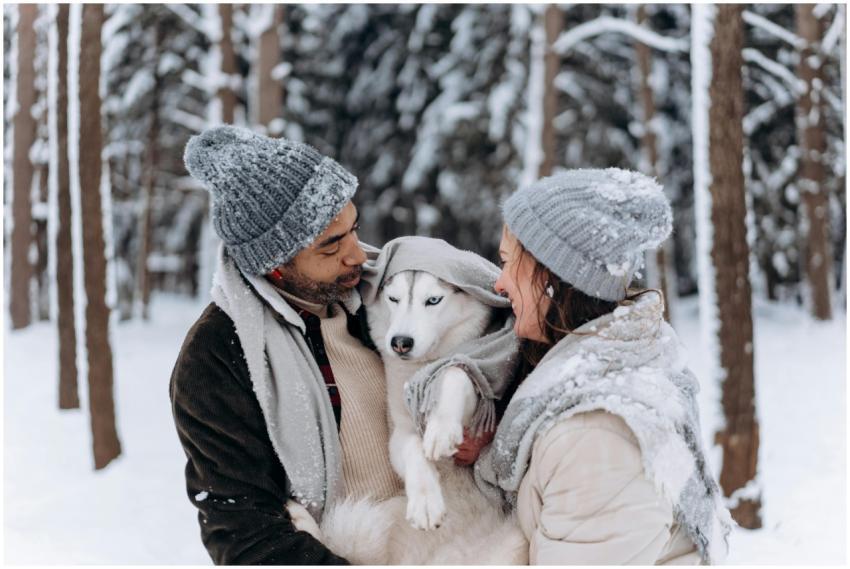 A couple in winter clothing embraces their husky d