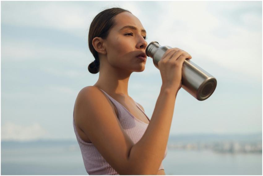 A woman drinks from a metal bottle on a sunny day