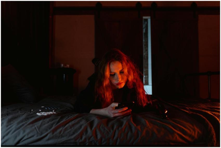 A young woman lying on a bed in a dark room, engro