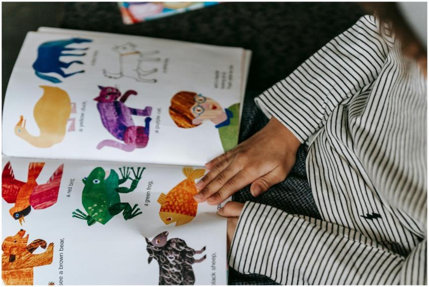 From above of crop anonymous child reading interes