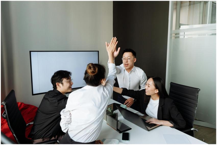 A group of Asian colleagues high-fiving in an offi