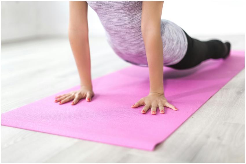 A woman performs a yoga stretch indoors on a pink