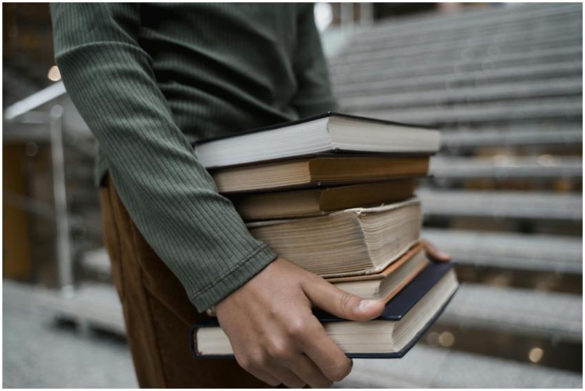 A close-up of a person carrying a stack of books w
