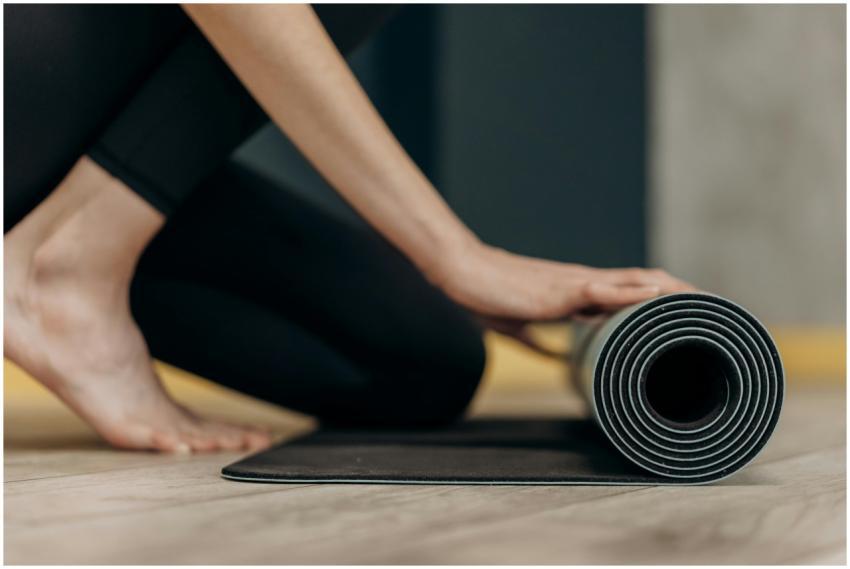 A young woman rolls up a yoga mat on a wooden floo