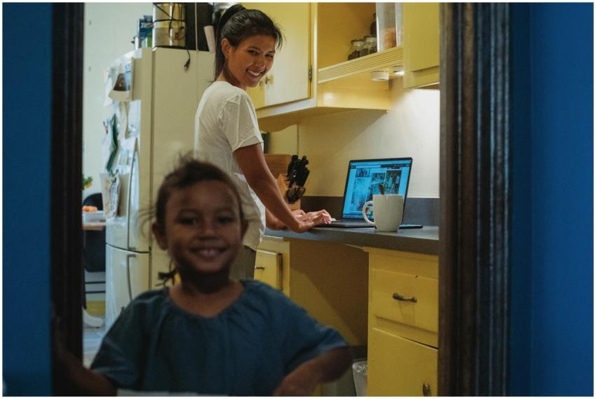 Cheerful ethnic woman browsing laptop in kitchen w