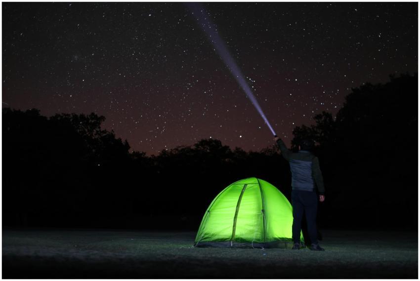 A lone camper observes the starlit sky near a glow