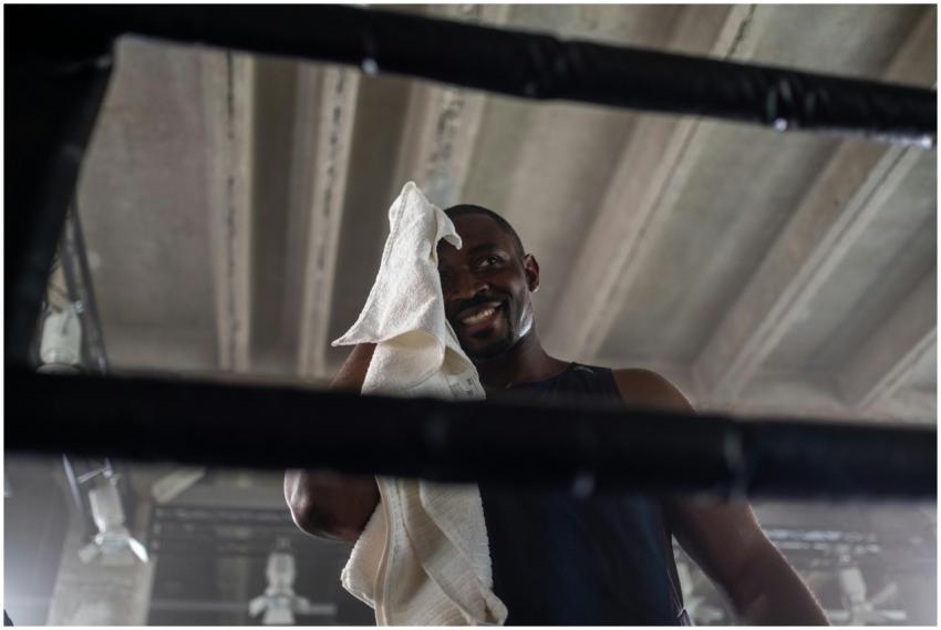 A smiling boxer wipes sweat with a towel in an ind
