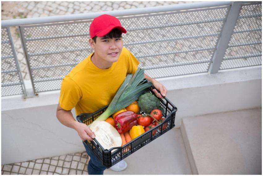 Young man holding a crate of fresh vegetables outd