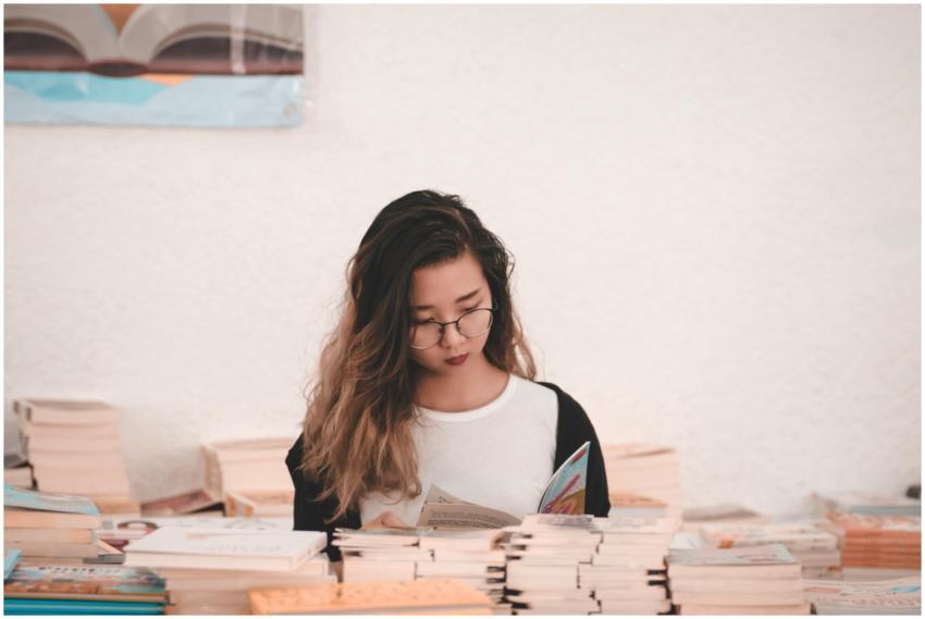 Asian woman engrossed in reading, surrounded by bo