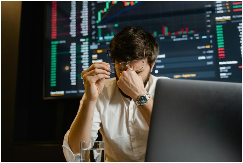 A stressed man looks at stock market data on his c