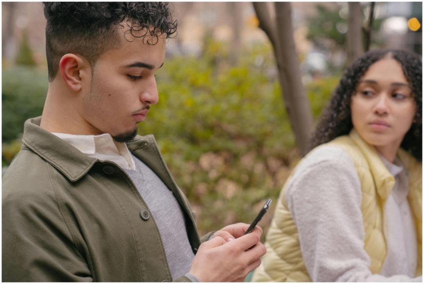 A young couple sitting outdoors with a smartphone,