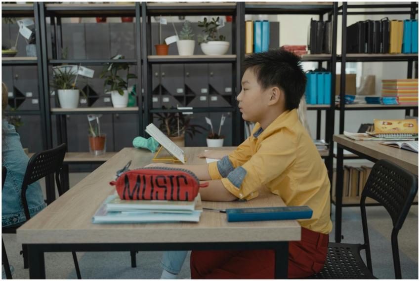 Boy in yellow shirt reading in a classroom with bo