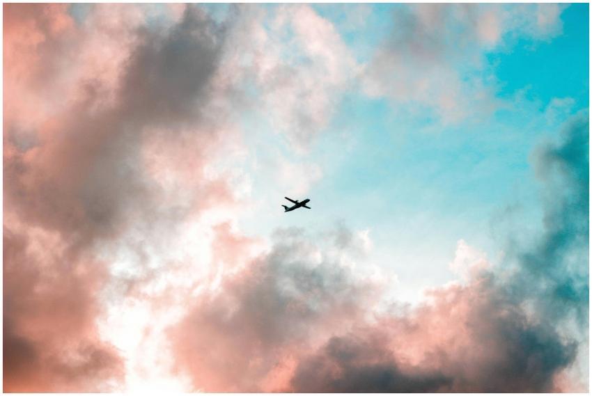 A plane flying through a colorful sky with pink an