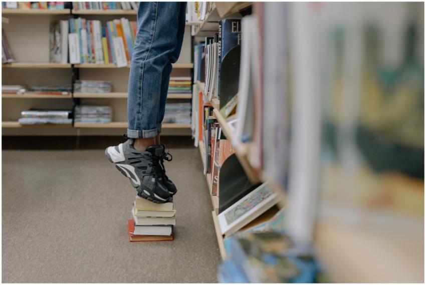 Person standing on stacked books in a library, rea