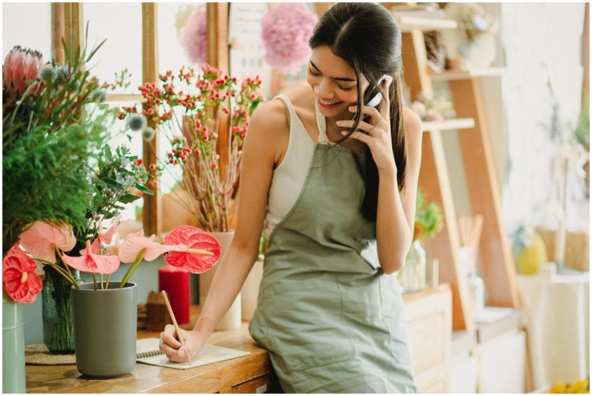 Female florist in apron on phone, writing notes in
