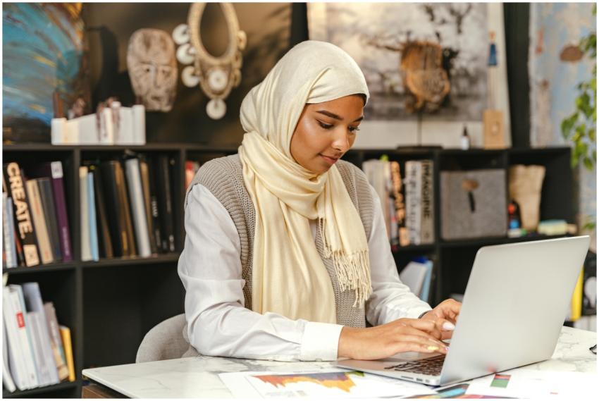 A Muslim woman in a hijab working on a laptop in a