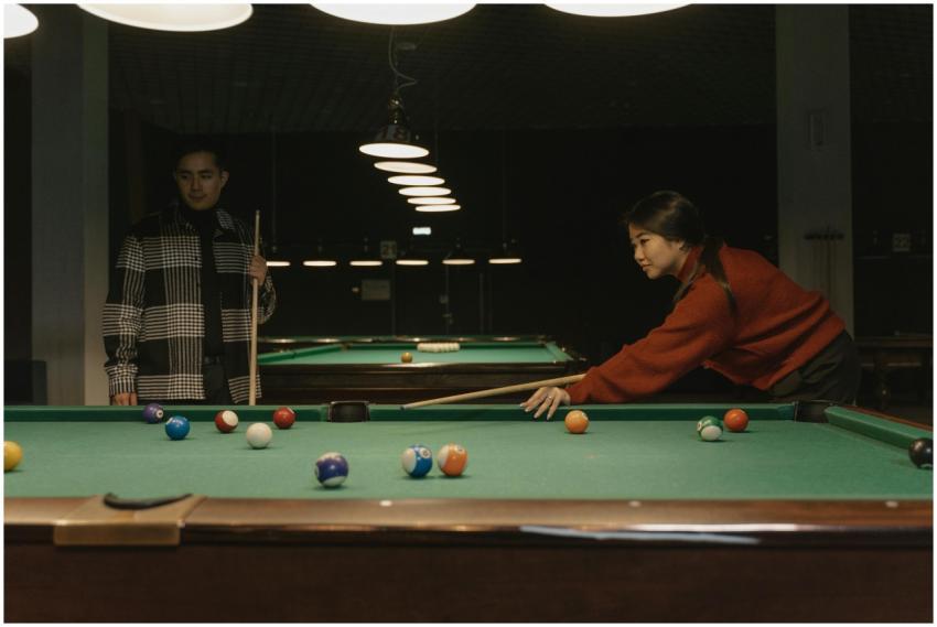 Two young adults enjoying a game of billiards in a