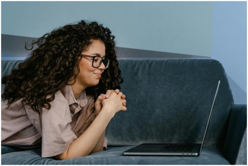 Woman with glasses lying on a sofa working remotel