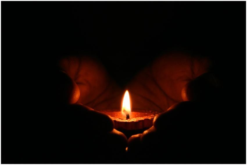 Close-up of hands warmly embracing a lit candle in