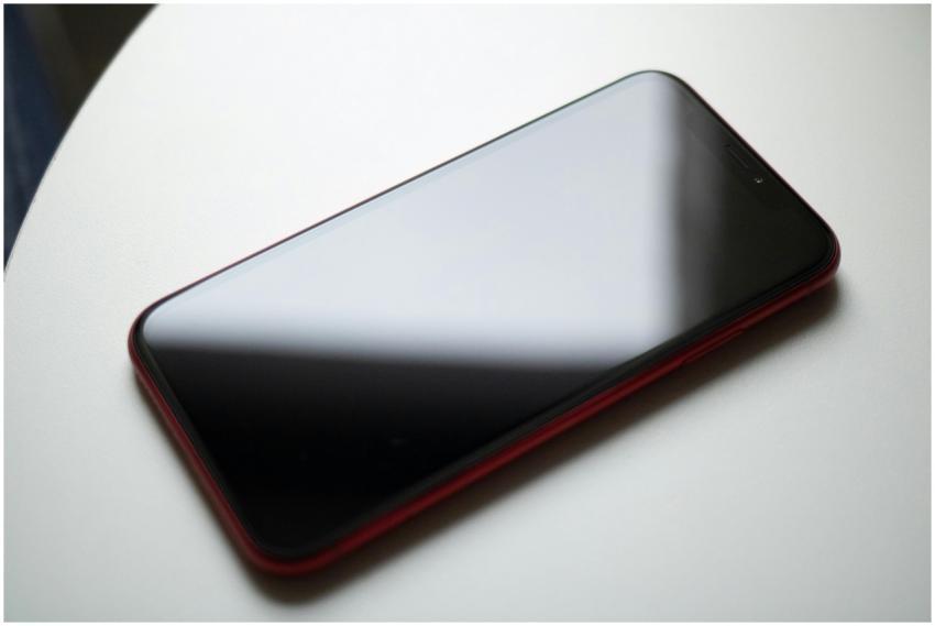 A sleek red smartphone placed on a white table sho
