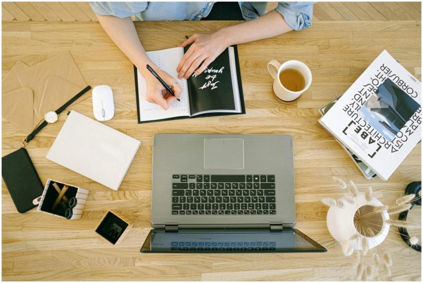 A woman writing notes at a home office desk with a