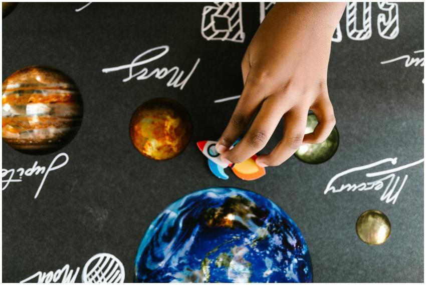 Child's hand arranging model planets on a space-th