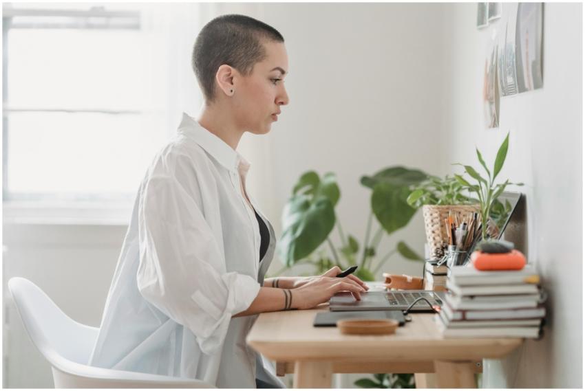 Woman using laptop at home office, surrounded by p