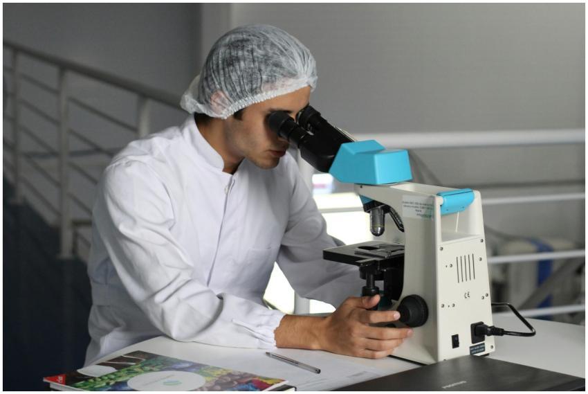 Scientist in a lab coat using a microscope to cond