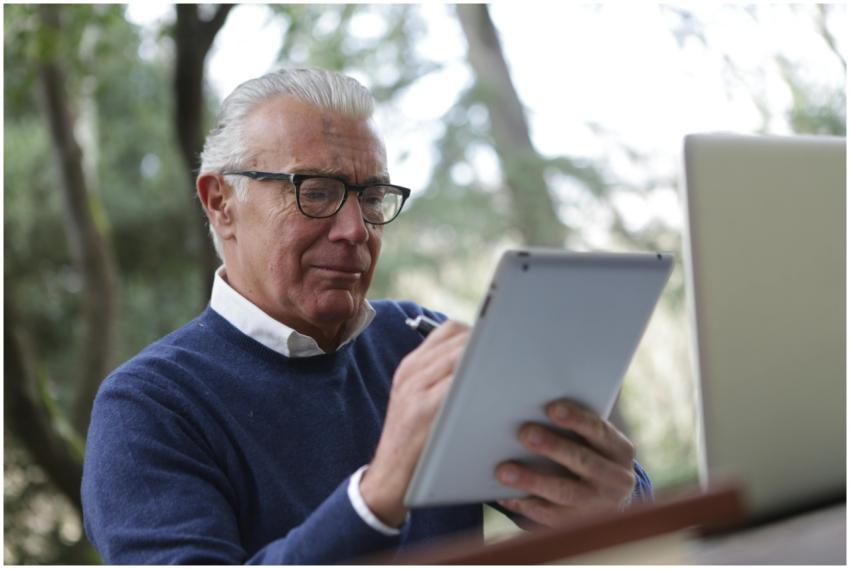 Elderly man using a tablet and laptop in an outdoo