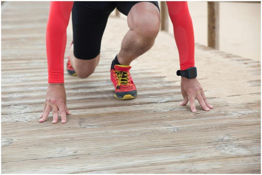Athlete in red gear gets ready to sprint on a wood