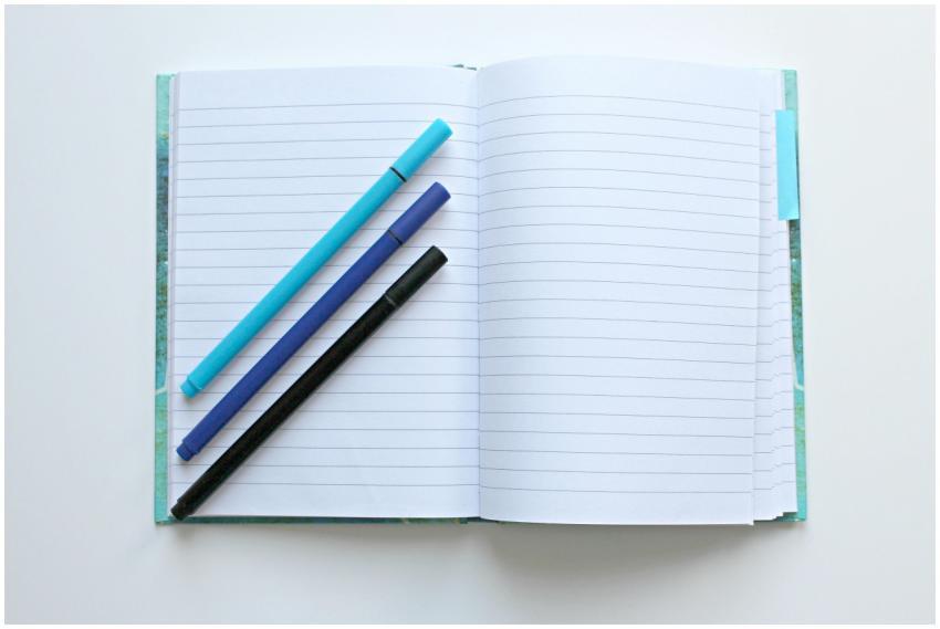 Open lined notebook with colorful pens on a white