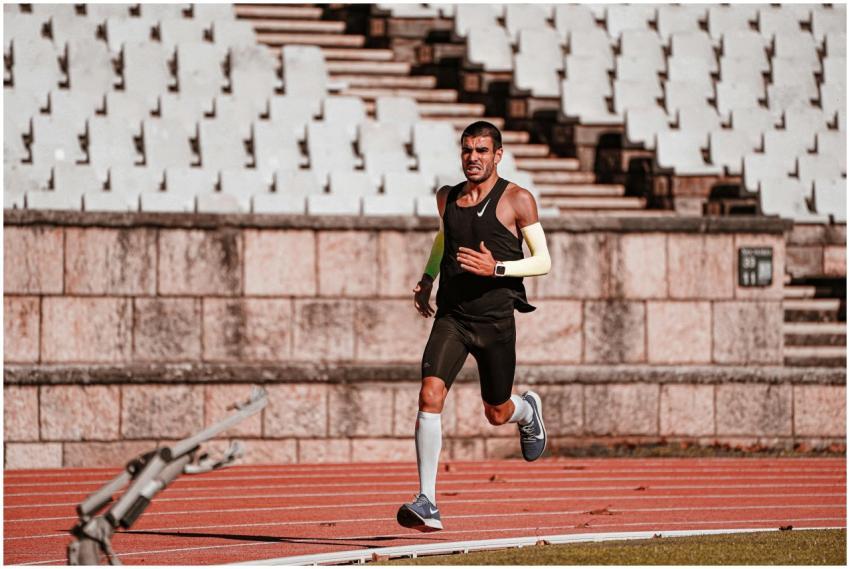 A determined male athlete runs on a track in a sun